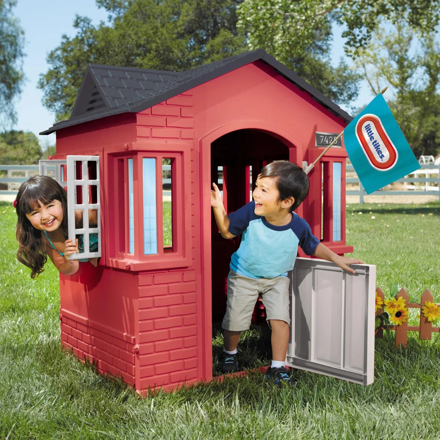Children playing in a red playhouse with a Little Tikes sign in the background.